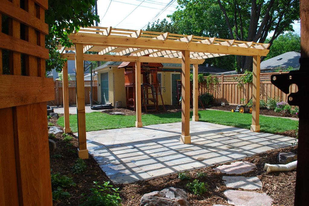 Finished cedar pergola over a bluestone patio in a residential backyard